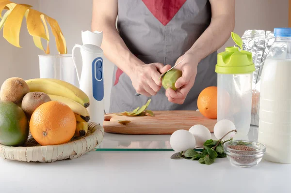 El chef está pelando el kiwi. Un hombre con un cuchillo en las manos limpia fruta. El cocinero de la cocina prepara un cóctel.. Imagen De Stock