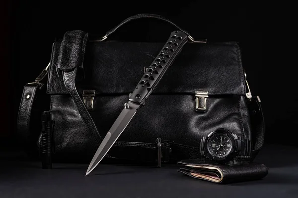 Cuchillo plegable grande y bolso de cuero negro. Cuchillo y reloj táctico. Objetos negros sobre fondo negro. CDE. — Foto de Stock