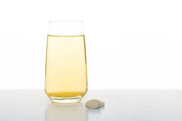 Verre à eau jaune. Boisson vitaminée dans un verre. Un verre et une tablette sur fond blanc. — Photo