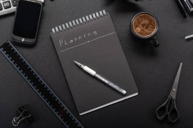 Görevler ve planlama. Gelecek planları. Siyah defter ve beyaz kalem. Not defteri ve kahve. Masadaki kırtasiye malzemesi.