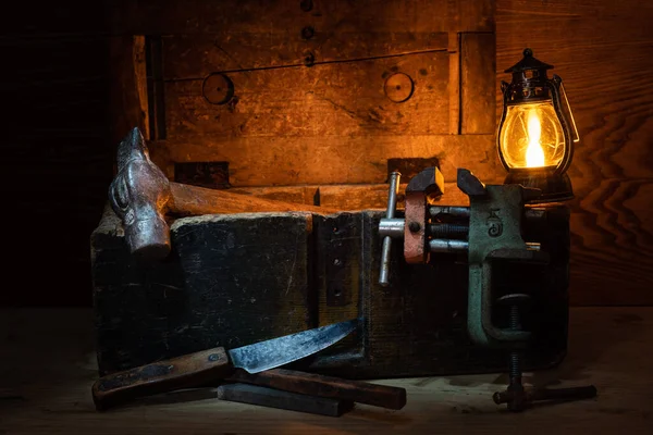 Bodegón de herramientas. Cuchillo viejo, martillo y vise. Una vieja caja de herramientas. Bodegón en secreto. Lámpara y vela sobre la mesa. . —  Fotos de Stock