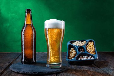 Bir şişe bira ve bir bardak bira. Damlalı soğuk bira. Köpüklü bir bardak bira. Çeşitli çerezler. Yeşil arka planda parlak bir bira.