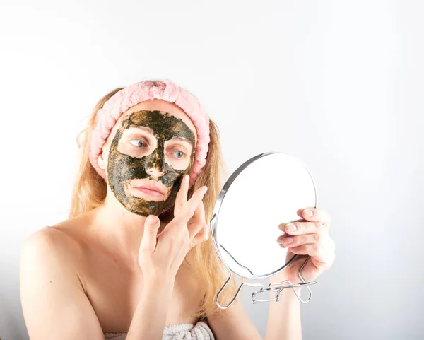 Girl apply a mask on her face. A woman with a mask on her face. Applying herbal face mask. Girl with a mirror. Girl in front of a mirror.