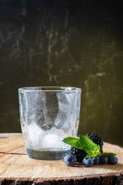 Buzlu boş bardak. Böğürtlen ve yabanmersini. Böğürtlen ve nane. Tahta bir kürsüde bir bardak ve böğürtlen. Dikey çerçeve.