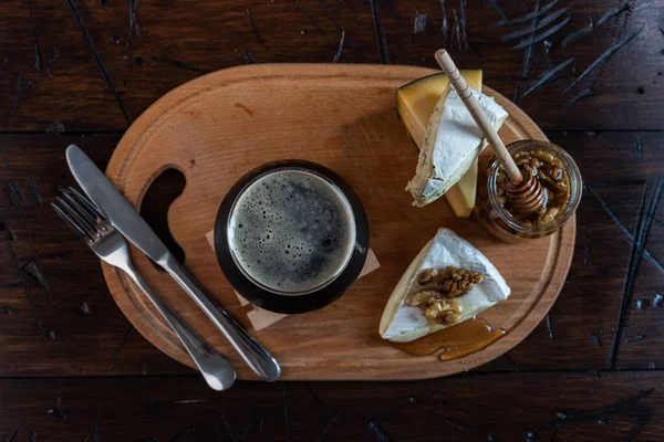 A glass of foamy black beer and cheese with honey. Cheese, honey and beer on the table. View from above. Beer composition.