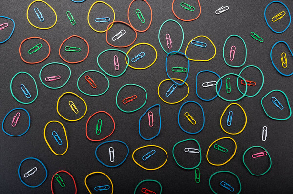 Текстура и фон скрепки и резинки. Много кругов на заднем плане. Заставка из офиса на черном фоне.