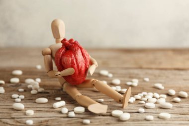 Oyuncak adam elinde anatomik bir kalp tutuyor, hapların yanına oturuyor. Kardiyovasküler sistem tedavisi, kalp krizi önleme.