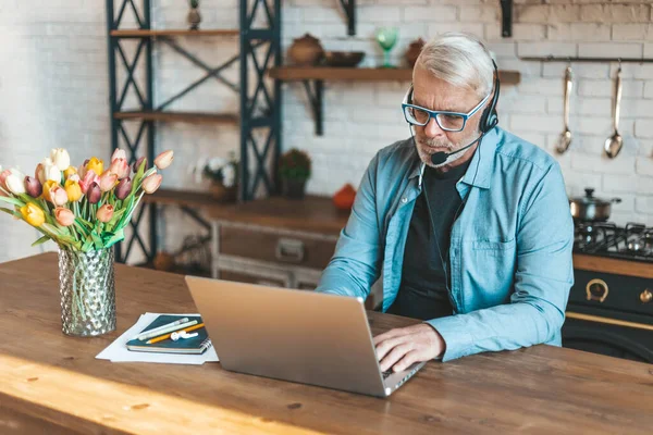 Kıdemli adam mutfaktan video ile iletişim kuruyor. Uzaktan muayene, evden çalışma. Kişisel online eğitim.