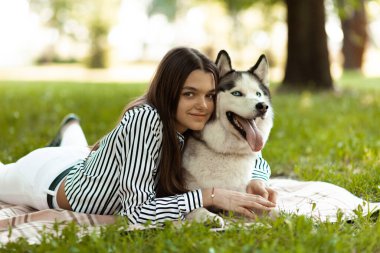 Genç bir kız parkta bir köpekle kucak kucağa yatıyor. Husky love, al bir evcil hayvan.