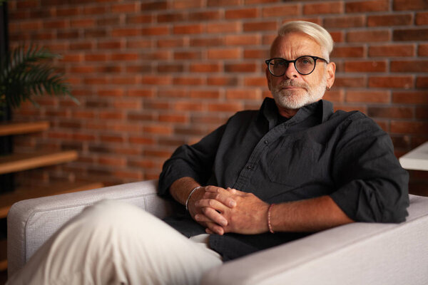 Portrait of a confident gray-haired man. Handsome pensioner relaxes in a chair. Luxurious retirement life.