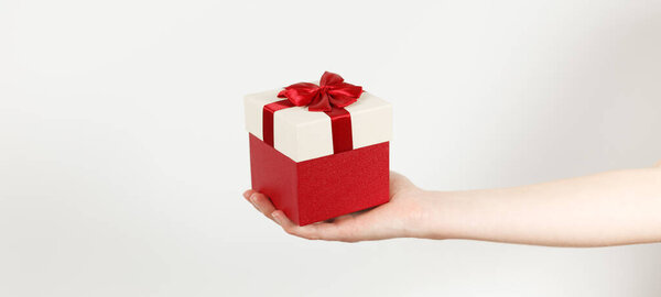 Red gift with a bow in hand on a white background. Anniversary present, Valentine's Day surprise.