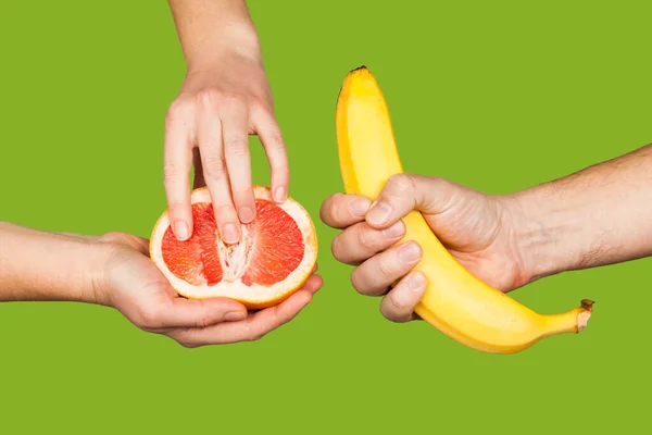 Banana and grapefruit in hands isolated on a green background as a symbol of male and female masturbation. Games with the clitoris and touching the penis. Stimulation and orgasm.