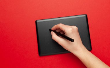 Kırmızı arkaplanda çizim ve tasarımcı eli için grafiksel tablet. Yaratıcı sanat, taslak.