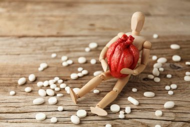 Oyuncak adam elinde anatomik bir kalp tutuyor, hapların yanına oturuyor. Kardiyovasküler sistem tedavisi, kalp krizi önleme.