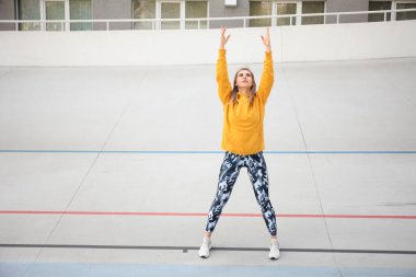 Sarı bluzlu ve askeri taytlı güzel kadın açık hava sporlarından önce ısınıyor..