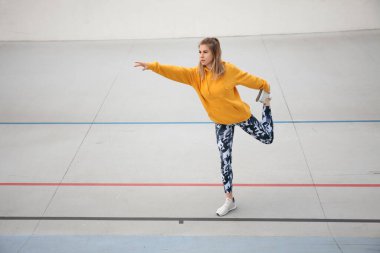 Sarı bluzlu ve askeri taytlı güzel kadın açık hava sporlarından önce ısınıyor..