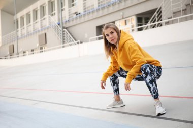 Sarı bluzlu ve askeri taytlı güzel kadın açık hava sporlarından önce ısınıyor..