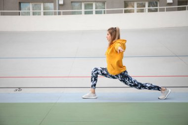 Sarı bluzlu ve askeri taytlı güzel kadın açık hava sporlarından önce ısınıyor..