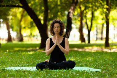 Kadın sabahları parkta temiz havada yoga yapıyor. Lotus pozu.