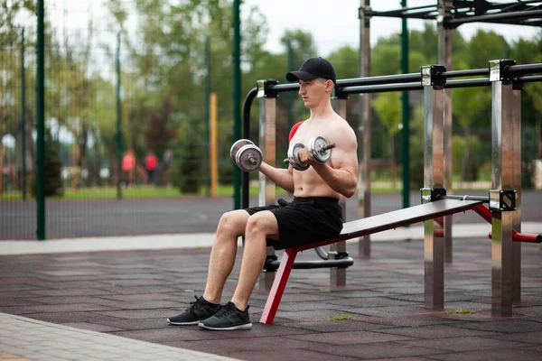 Young European athlete with injury is training outdoors. Kinesiology ( therapeutic, Kinesio, k-tape, KT, physio) tape on shoulder. Rehabilitation and recovery. Exercise with dumbbells.