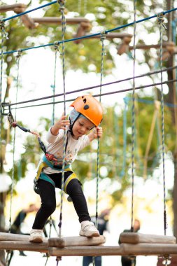 Miğferli küçük kız dışarıdaki macera parkında iplere tırmanıyor. Olağanüstü spor, doğada aktif eğlence..