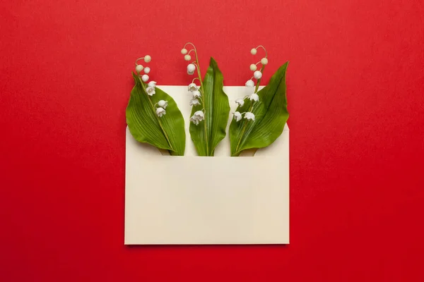 May fresh lily of the valley in a mail envelope on a red background. Wedding invitation concept, romantic letter.