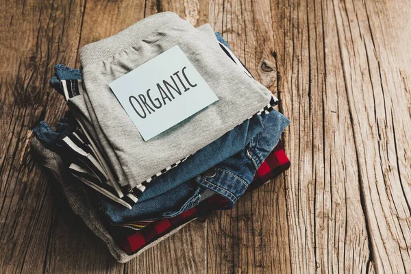 Stack of organic clothes on a wooden background. Natural eco-friendly fabric.