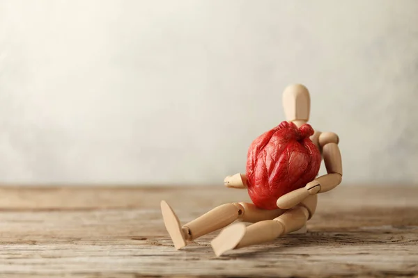 Wooden toy man holds a heart. Donor and transplant, symptoms of an attack. Surgical Assistance