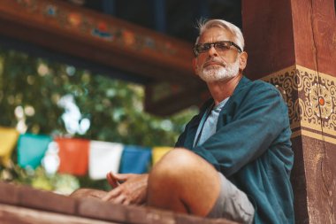 An elderly European tourist meditates in an Asian temple. A pensioner tourist is resting in an old monastery. Calmness, pacification and enlightenment.