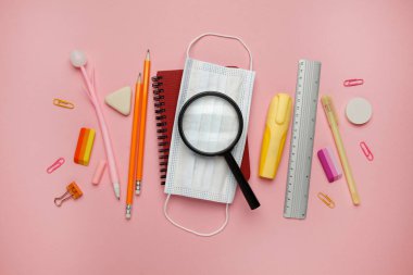 Pembe arka plan üzerinde çalışmak için yüz maskesi ve kırtasiye malzemesi. Karantina kısıtlamaları, korunma ve hastalıkların önlenmesi. Bir salgın sırasında çalış.