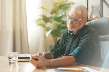 Yüksek tansiyonun önlenmesi. Yaşlı adam masadaki baskıyı ölçer. Yaşlılıkta sağlığa önem vermek..