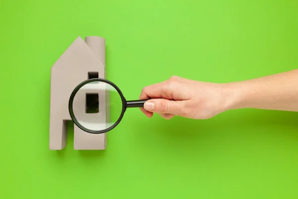 Search for real estate. Hand with a magnifying glass and a toy house on a green background. Choosing an apartment for rent.