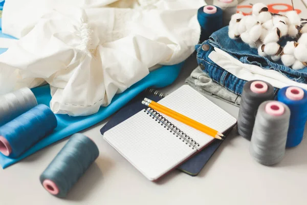 Clothing repair. Workplace of a seamstress, threads with fabrics and a notebook on the table. Tailoring service.