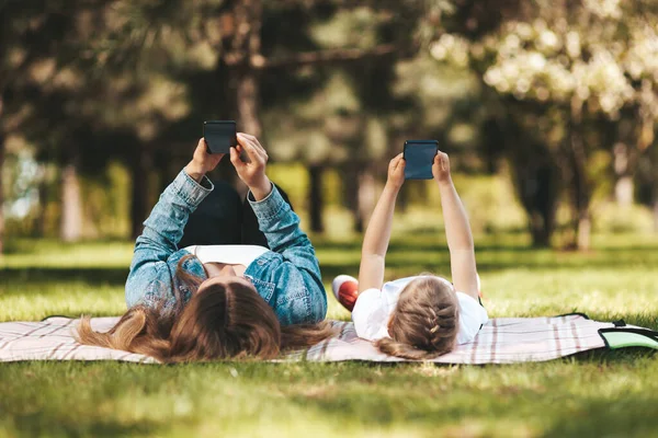Smartphone addiction. People lie in the park with phones in their hands. Using gadgets, chat with friends, mobile gaming.