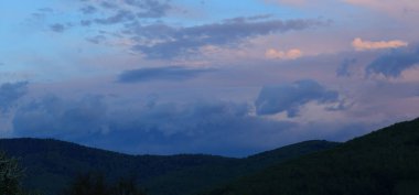 Alacakaranlık, akşam vakti. Dağların üzerinde bulutlarla gün batımı.