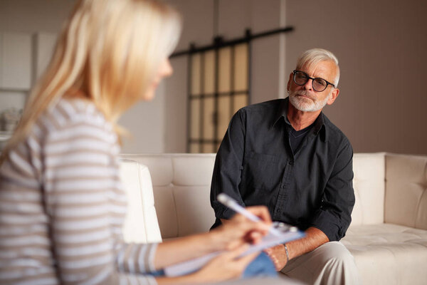 Comfortable psychotherapy. An elderly patient with a problem,  session with a psychologist. The doctor listens and writes down the diagnosis.