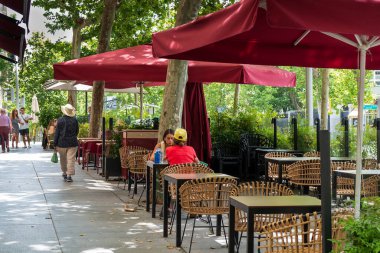 Madrid, Spain -- June 17, 2022. A landscape photo with two women having drinks at an outdoor cafe while tourists walk in the background.