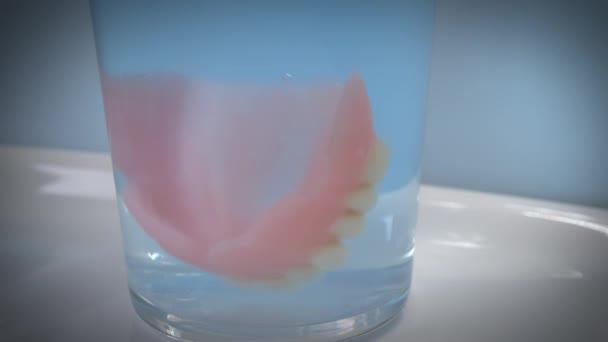 Κοντινό πλάνο του βάζοντας οδοντοστοιχίες σε ένα ποτήρι νερό καθαρισμού. — Αρχείο Βίντεο
