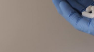 Mavi lateks eldivenli, elinde beyaz haplar olan bir elin yakın plan fotoğrafı..