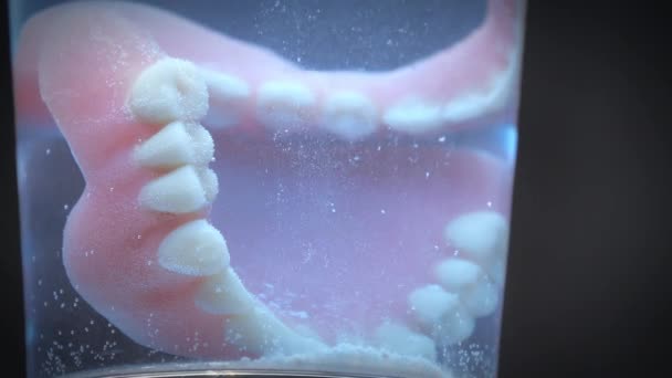 Κοντινό πλάνο που δείχνει οδοντοστοιχίες σε ένα ποτήρι υγρό καθαρισμού. — Αρχείο Βίντεο