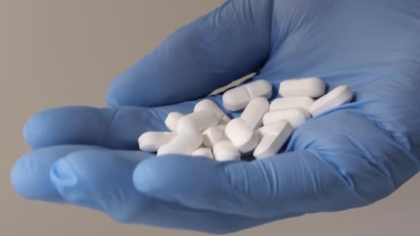 Primer plano de una mano en guantes de goma azul sosteniendo píldoras blancas. — Vídeos de Stock