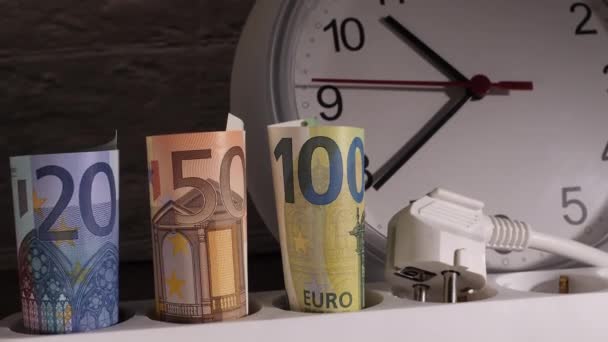Close-up tiro de dinheiro em uma tomada elétrica com um relógio atrás deles. — Vídeo de Stock
