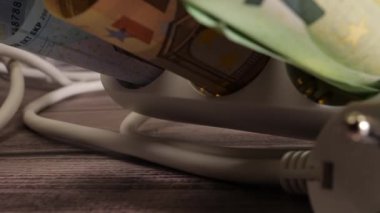 Yakın çekim para ve yüksek elektrik fiyatı kavramını gösteren bir soket.