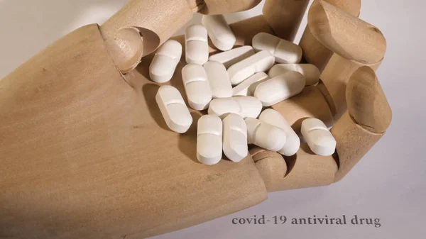 Tahta bir elin üzerinde beyaz hapların yakın plan çekimi. Beyaz arka plan. Siyah metin.