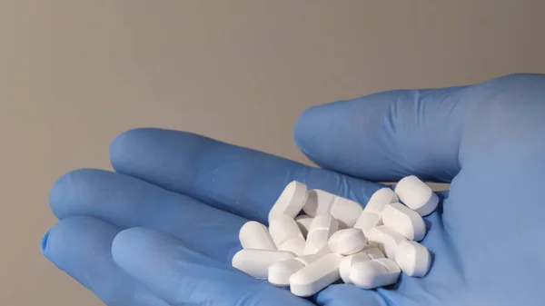Beyaz haplar tutan lateks eldivenli bir elin yakından çekimi. Eczacılık. 