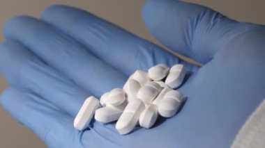 Elinde haplar tutan mavi lastik eldivenli bir elin yakından çekimi. Beyaz arka plan. İnsanlara ilaç konseptini vermek. İlaç sanayisi. Haplar elden düşer..