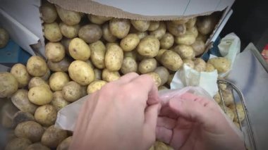 Closeup shot showing the difficulty of opening a plastic bag in a supermarket. Grocery shopping. Potatoes in the background.