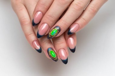 Yeşil taşlı altın broşlu mavi Fransız manikürü.