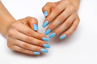 Açık mavi manikür kare uzun çiviler üzerinde kristaller beyaz arka planda yakın plan.