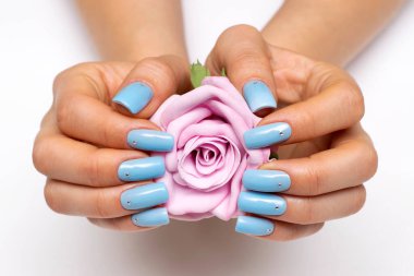 Açık mavi manikür, ellerinde pembe bir gül ve beyaz arka planda kristallerle kare uzunluğunda çiviler..